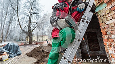 Worker in protect gloves is holding the hand screwdriver on the ladder in construction site. Concept of using of Stock Photo