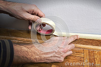 Worker protecting batten moulding with masking tape before paint Stock Photo