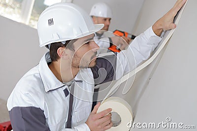 Worker protecting batten moulding with masking tape before painting Stock Photo
