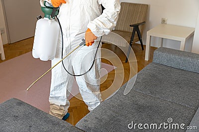 Worker in protective suit with decontamination sprayer bottle disinfecting household and furniture. Pest control concept. Stock Photo