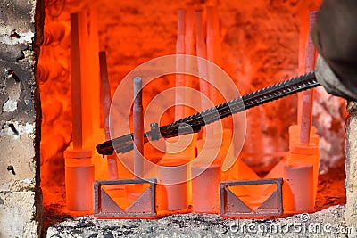 Worker pulls out the heated parts with tongs from an electric furnace for hardening metal. Dangerous work with high Stock Photo