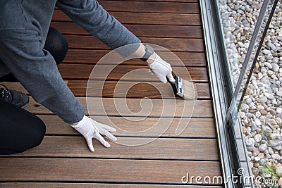 Worker refinishing wood, hand painting wooden deck floor with wood protection oil Stock Photo