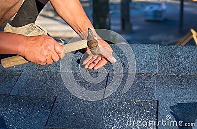 Worker repair corner bitumen roof shingles with hammer and nails Stock Photo