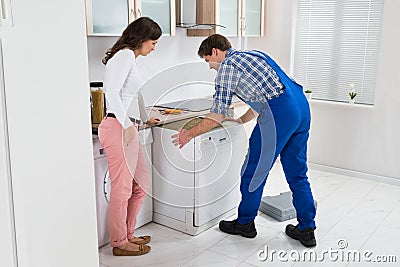 Worker Repairing Dishwasher While Woman In Kitchen Stock Photo