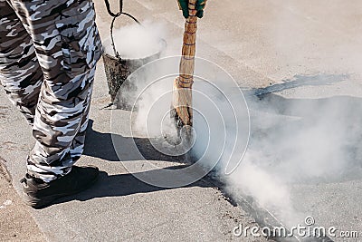 Worker repairs the roof with molten tar from a bucket with a broom Stock Photo