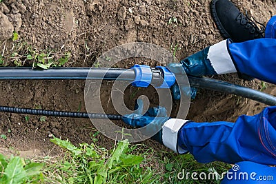 Worker`s hands hold a black pipe over a dug hole in the ground Stock Photo