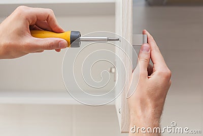 The worker sets a new handle on the white cabinet with a screwdriver. Stock Photo