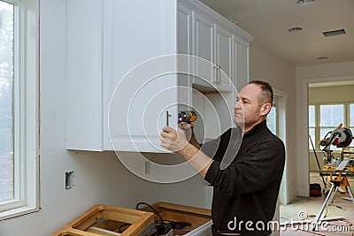 Worker sets a new handle on the white cabinet with a screwdriver installing kitchen cabinets Stock Photo