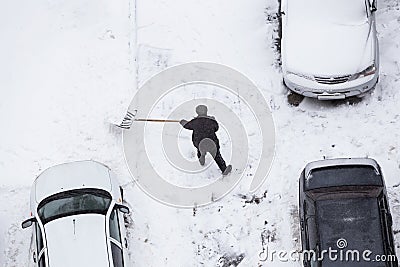 Worker shoveling snow after snowfall on road, parking near car Stock Photo