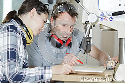 worker showing female apprentice how to use bench drill Stock Photo