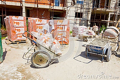 Worker is taking off hook of crane from wheelbarrow full of waste, plastic foil, works on building site Editorial Stock Photo
