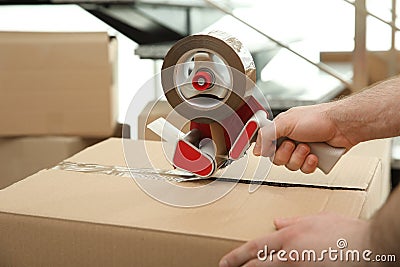 Worker taping cardboard box indoors, closeup view Stock Photo
