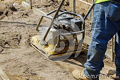 Worker use vibratory plate compactor under construction on new pavement Stock Photo