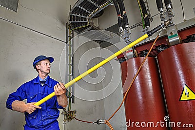 Worker uses insulating stick to earth grounding transformer. Stock Photo