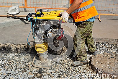 A worker uses a portable vibration rammer during road repairs. Stock Photo