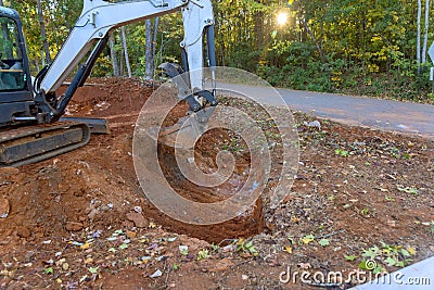 Worker uses tractor to excavate ditch for laying drainage conduit Stock Photo