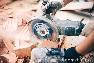 Worker using grinder on construction site for cutting bricks, debris. Tools and bricks on new building site Stock Photo