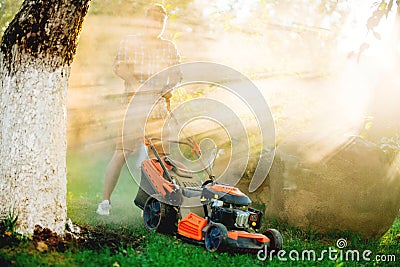 Worker using industrial lawnmower against direct sunlight, details of landscaping and gardening Stock Photo