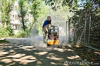 Worker with vibratory plate compacts sand before laying paving slabs in Perm, Russia Editorial Stock Photo