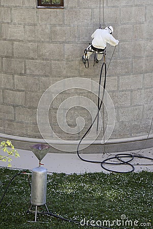 Worker wearing a protective gear cleaning a stone faceade in rope access Stock Photo