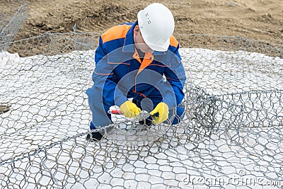 Worker in a white helmet and overalls knits a steel wire structure Stock Photo