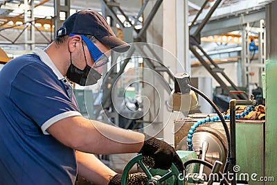 A worker worries about his safety during quarantine while wearing an anti-covid 19 mask. A turner works on metal-working equipment Stock Photo