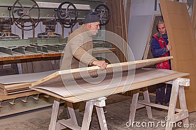 Workers in carpentry line up glued wooden profiles before pressing in the large clamp machine Stock Photo