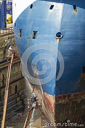 Workers cleaning impurities and removing paint with a pressure sandblasting from the hull of a merchant ship Stock Photo