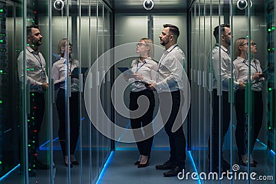 Workers in a data center walking between rows of server racks Stock Photo