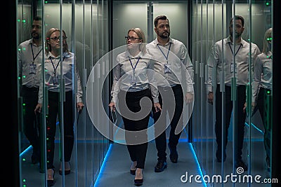 Workers in a data center walking between rows of server racks Stock Photo