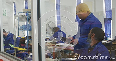 Workers discussing about the work. Side view of an African American male worker and a mixed male worker in a workshop at a factory making wheelchairs, one of stock video Workers discussing about the work. Side view of an African American male worker and a mixed male worker in a workshop at a factory making wheelchairs, one of stock video
