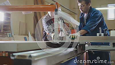 Workers at factory are cutting wooden fragment on electric saw at furniture industry Stock Photo