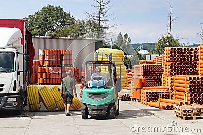 Workers with forklifts in a warehouse of plastic pipes. Sale of materials for construction and upgrading of the territory. Industr Editorial Stock Photo