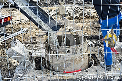 workers handling massive cement pump tube and pouring fresh concrete on reinforced bars at new construction site Stock Photo