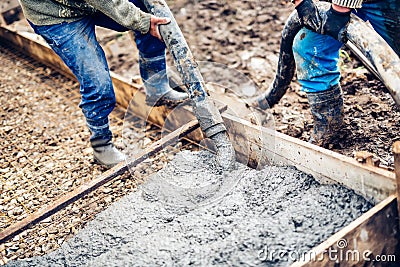 workers handling massive cement pump tube and pouring fresh concrete on reinforced bars at new construction site Stock Photo