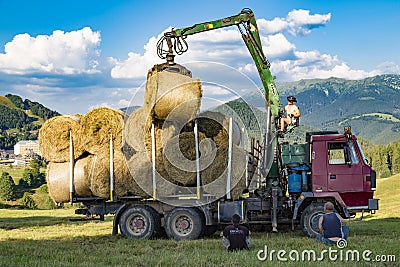 Workers load round hay bale from mown grass to a truck. Tatras Editorial Stock Photo