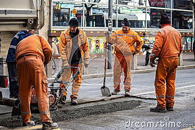 Workers in orange uniforms and protection equipment fixing and patching damaged road Editorial Stock Photo