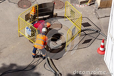 Workers over an open sewer manhole on the street, repairing pipes and underground utilities Editorial Stock Photo