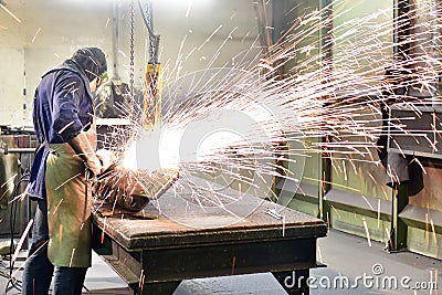 Workers in protective equipment in a foundry work on a casting with a grinding machine at the workplace Stock Photo