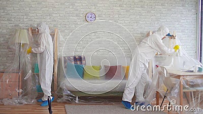 Workers In Protective Suits Cover The Furniture With Plastic Wrap