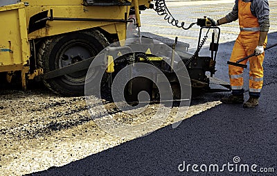 Workers regulate tracked paver laying asphalt Stock Photo