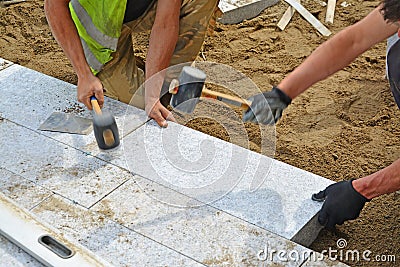 Workers tapping pavers into place with rubber mallets. Stock Photo