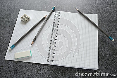Working desktop with a blank open spiral notebook, pencils, sharpener and eraser on a dark gray table, mock up with copy space Stock Photo