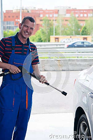 Working holds a gun in his hands to wash the car, and smiles Stock Photo