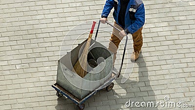 A working janitor comes with a trash cart and cleaning accessories: broom, dustpan. Stock Photo