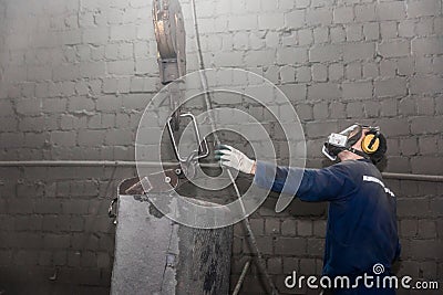 A working man in overalls and a respirator takes a hook with his hand lifting mechanism, equipment with cast iron reinforced Stock Photo