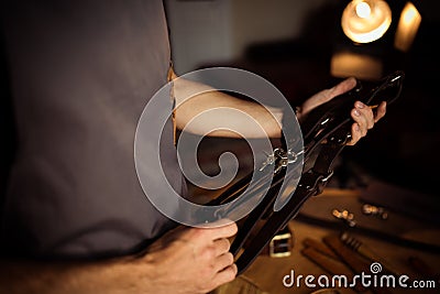 Working process of the leather belt in the leather workshop. Man holding photographer`s belt for camera. Tool on wooden Stock Photo