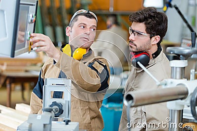 Workman explaining machinery controls to factory apprentice Stock Photo