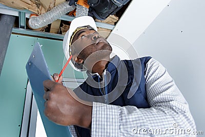 workman looking at ventilation system and making notes on clipboard Stock Photo