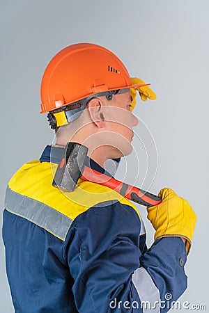 Workman in an orange helmet and with a hammer on his shoulder stands with his back to the camera on a gray background Stock Photo